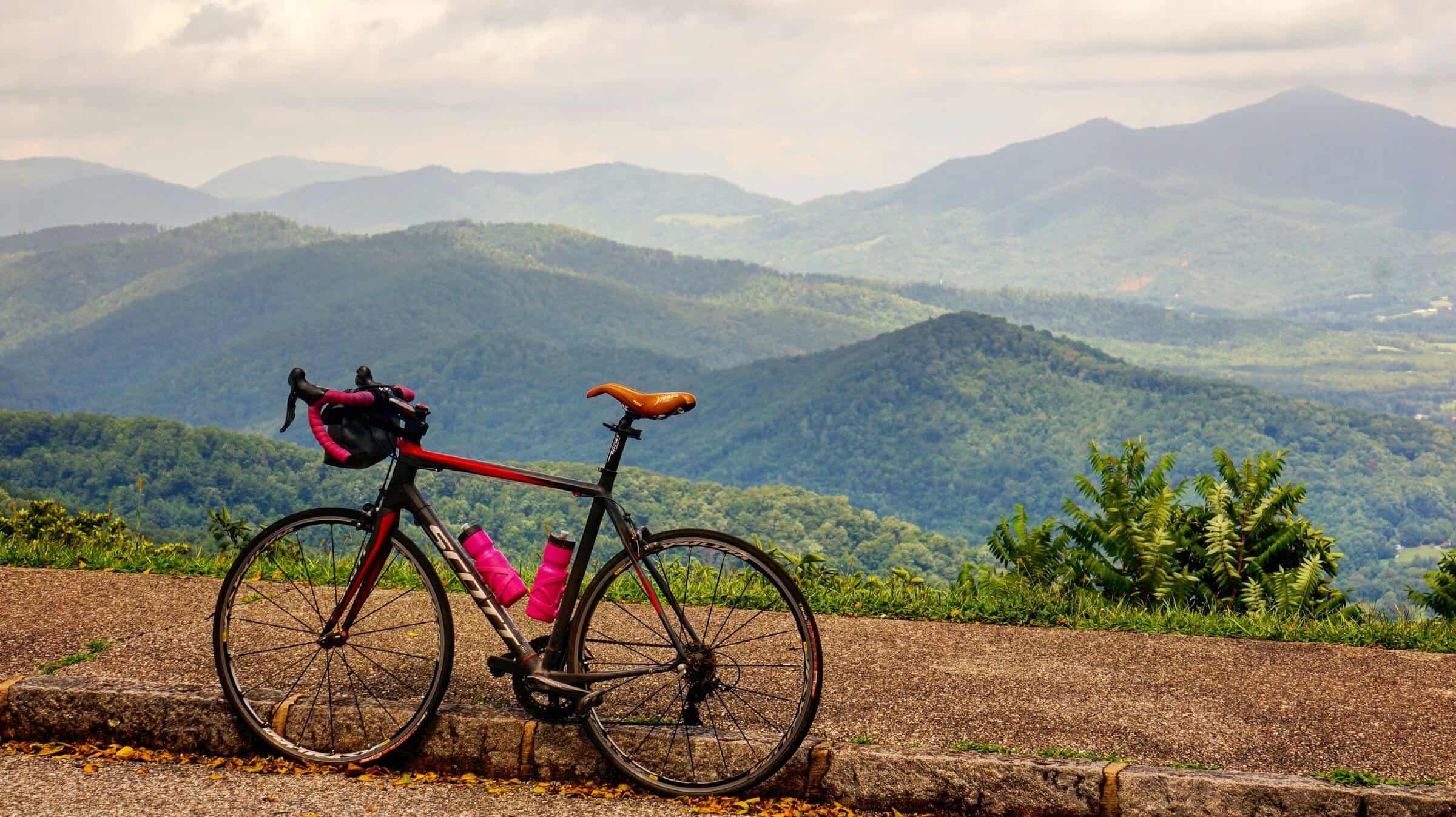 A bicycle standing by itself with rolling mountains in the background.