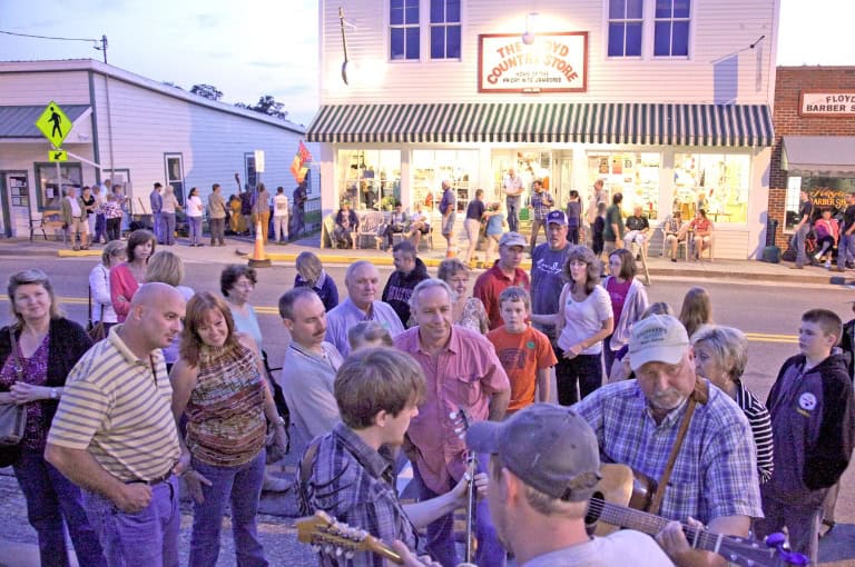 A crowd gathers around musicians performing outside on the sidewalk during dusk.