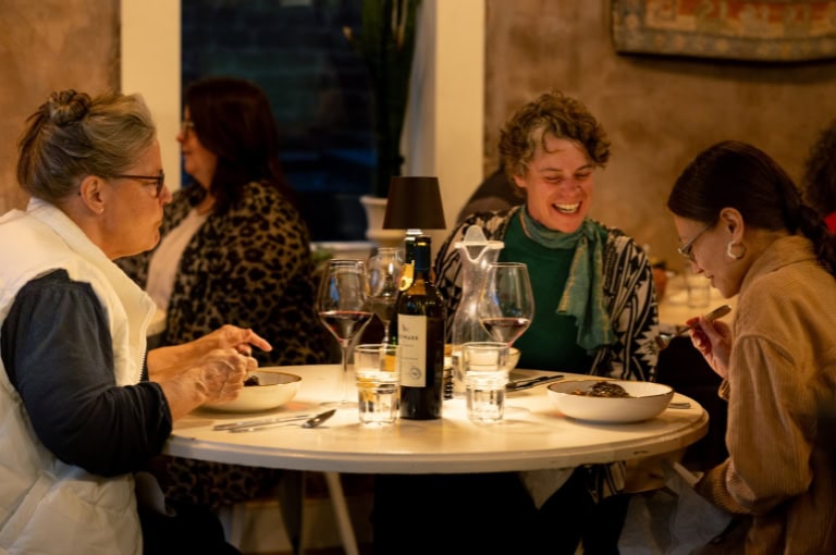 Three women sitting at a table in a cozy restaurant, enjoying dinner and wine.