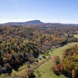 A panoramic view of a lush, hilly landscape with colorful autumn foliage under a clear blue sky.