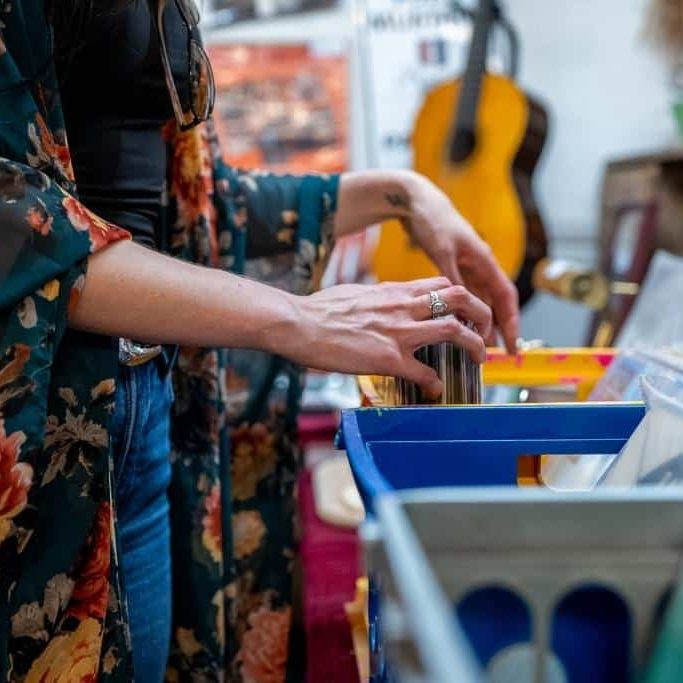 A person is browsing through vinyl records in a colorful crate, wearing a floral kimono and holding a record.